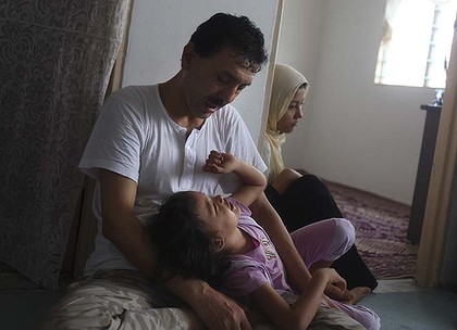 Hazara refugee Rajab plays with his eldest grandchild in the living room of their flat in Kuala Lumpur. Photo: Rahman Roslan 